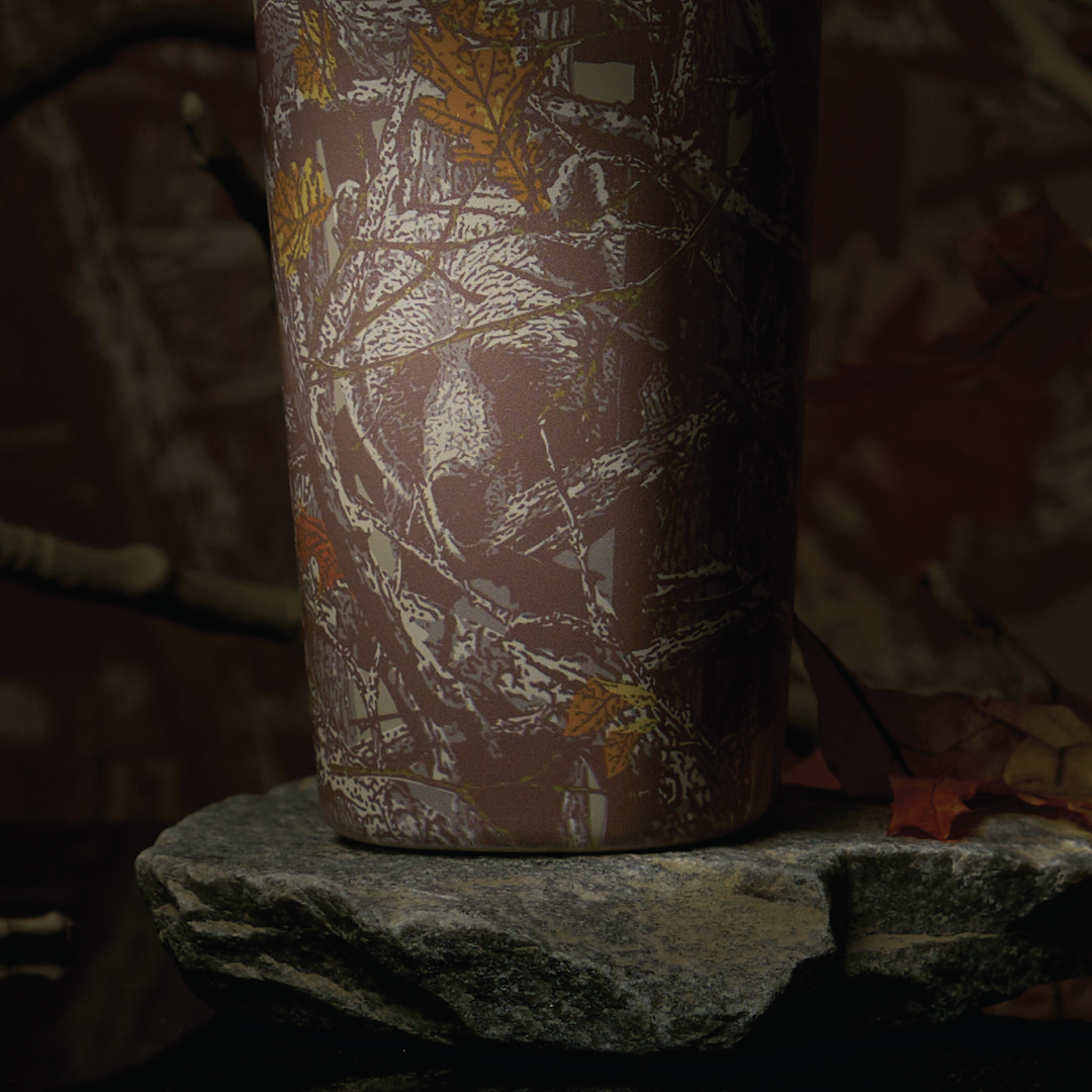 Owala FreeSip Sway in Out of Sight, back view of woodland camo patterned body shown on a rock in a forest setting